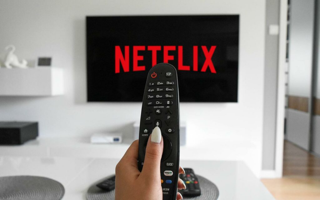 Hand pointing TV remote at screen displaying Netflix logo